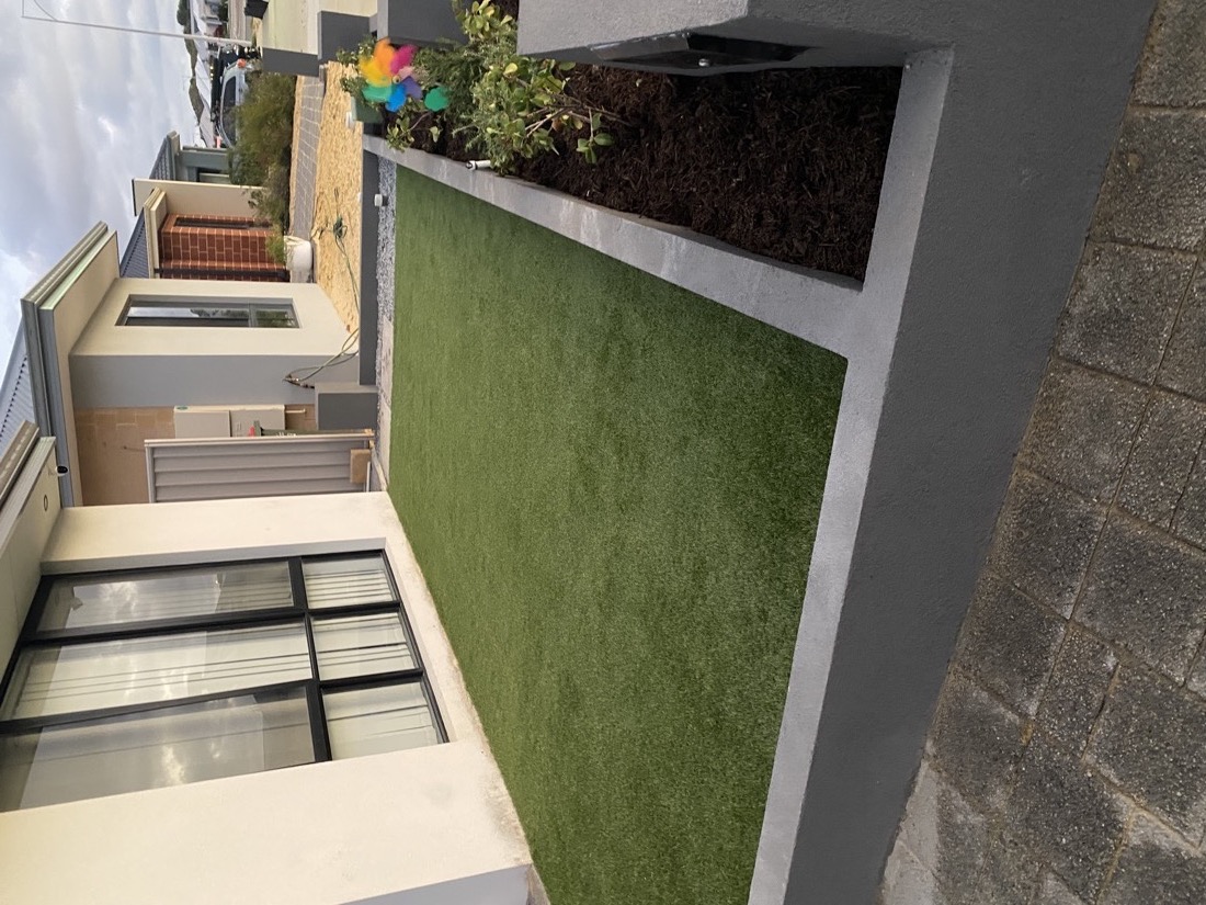 A tidy turf strip set into the same narrow side area, finished with crisp concrete edges.